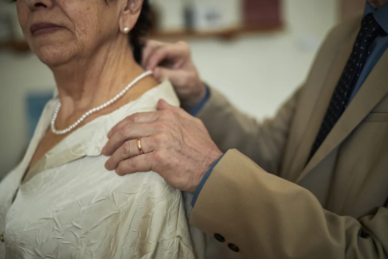 man adjusting necklace on elderly woman in white b 2025 08 27 06 39 18 utc